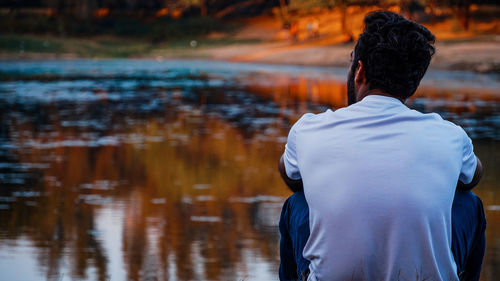 Rear view of young man sitting by lake