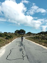 Rear view of person cycling on road against sky