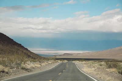 Empty road by mountains against sky