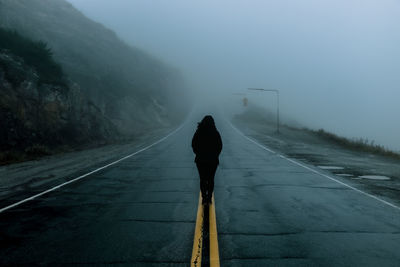 Rear view of woman standing on road during foggy weather