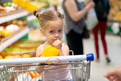 Cute girl holding yellow bell pepper at supermarket