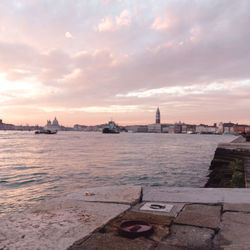 View of city at waterfront against cloudy sky