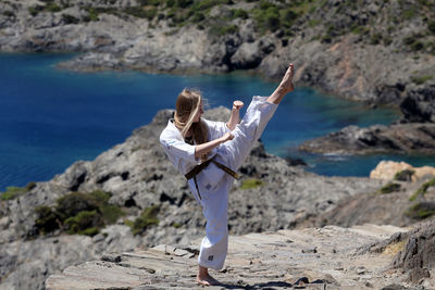 Full length of woman practicing karate on rock against sea