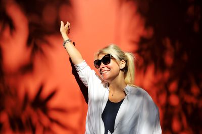 Happy woman wearing sunglasses while standing against wall