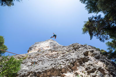 Low angle view of male friends climbing on mountain against clear blue sky