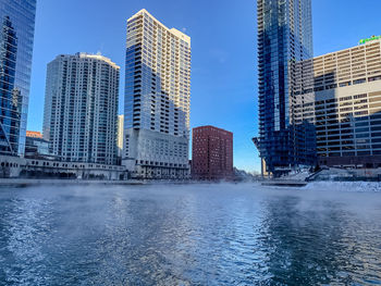 Modern buildings by river against sky in city