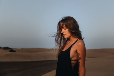 Side view of young woman standing in desert against sky