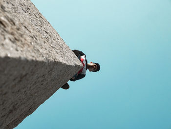 Low angle portrait of man standing on wall against clear blue sky