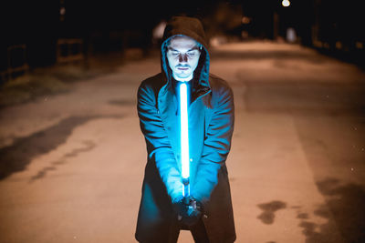 Portrait of young man standing against illuminated wall at night