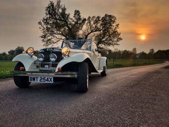 Car on road by field against sky during sunset