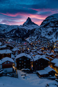 Snow covered buildings and mountains against sky at dusk