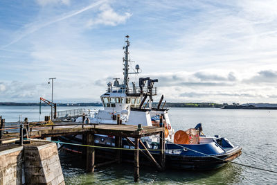 Fishing boats moored at harbor against sky