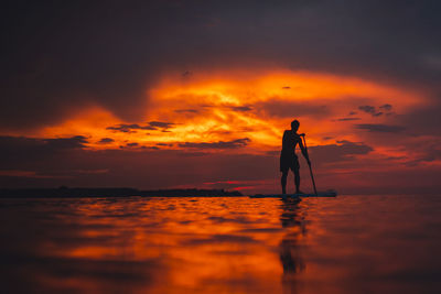 Silhouette man standing on paddleboard against sky during sunset