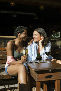 Happy multiracial female friends communicating while having wine at restaurant