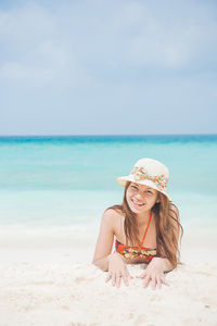 Portrait of woman wearing hat lying at beach against sky during sunny day