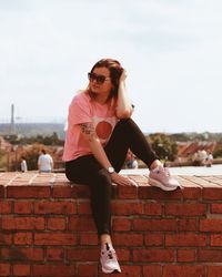 Young woman wearing sunglasses on brick wall