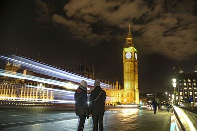 Rear view of people standing against big ben tower at night
