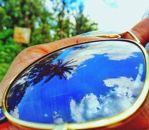 Close-up of hand on glass against sky