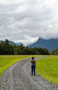 Rear view of woman walking on road against cloudy sky