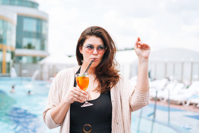 Stylish woman plus size body positive in black swimsuit with glass of cocktail near pool