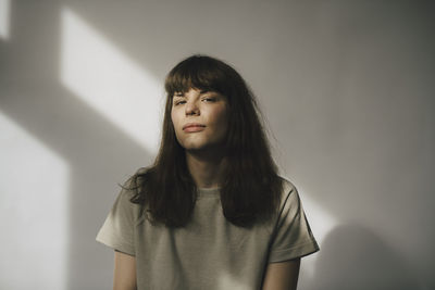 Portrait of young woman standing against wall at home