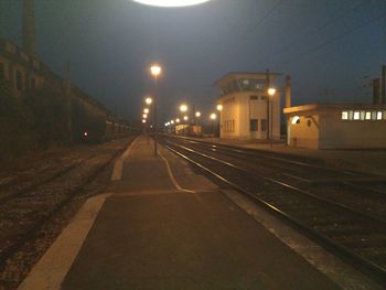 Illuminated railroad tracks amidst buildings in city at night