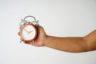 Close-up of hand holding clock against white background