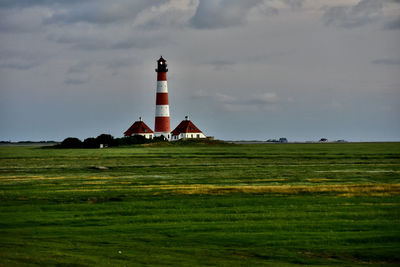 Lighthouse on field by building against sky