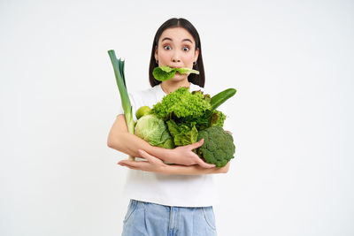 Portrait of smiling young woman holding vegetable against white background