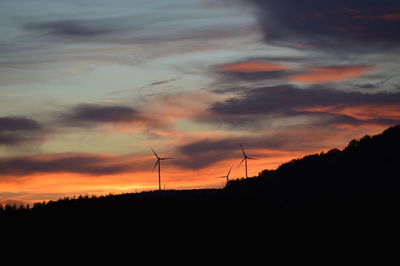 Silhouette of wind turbines against dramatic sky during sunset