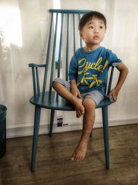 Boy looking away while sitting on chair at home