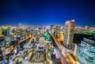 High angle view of illuminated city buildings against clear blue sky