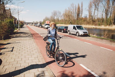 Woman riding bicycle on road against sky during sunny day