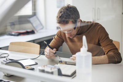 Focused engineer repairing machine part through soldering iron at workshop