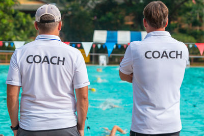 Rear view of men wearing t-shirts with coach text standing by swimming pool