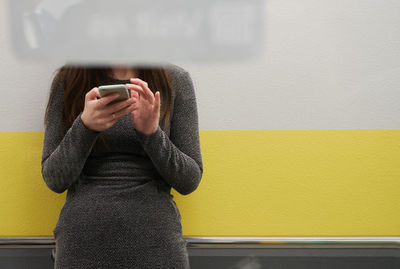 Midsection of woman using mobile phone while standing against wall