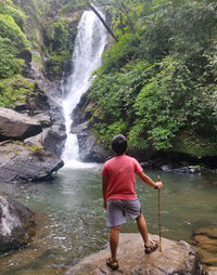 Full length rear view of man standing against waterfall