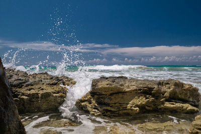 Waves splashing on rocks at shore against sky