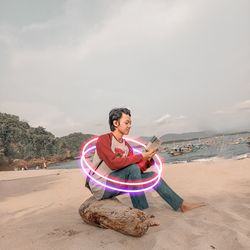 Man sitting on sand at beach against sky