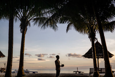 Silhouette man standing at beach against sky during sunset