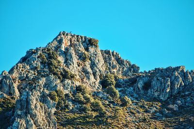 Low angle view of rocky mountains against clear blue sky