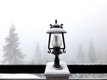 Close-up of electric lamp on glass against sky during winter