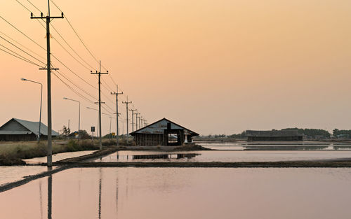 Houses by electricity pylon against clear sky during sunset