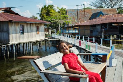 Portrait of girl smiling while sitting on bench over sea