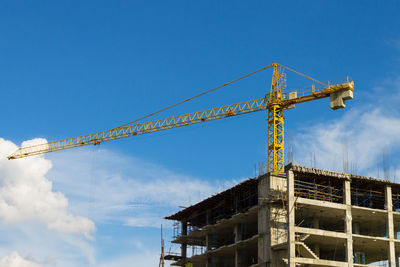 Low angle view of crane at construction site against sky