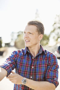 Man looking away while rolling up shirt sleeve on a sunny day