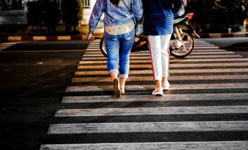 Low section of women walking on road in city