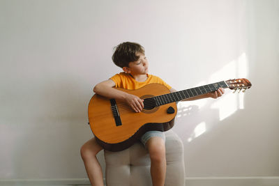 Cute boy learns to play the classical guitar in home. cozy home.