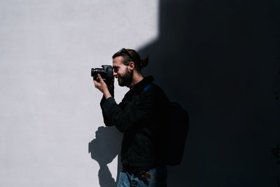 Smiling man taking pictures next to a black and white wall in the back