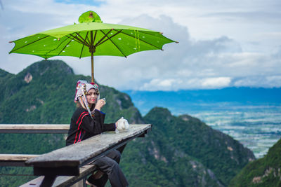 Woman sitting against mountain and cloudy sky